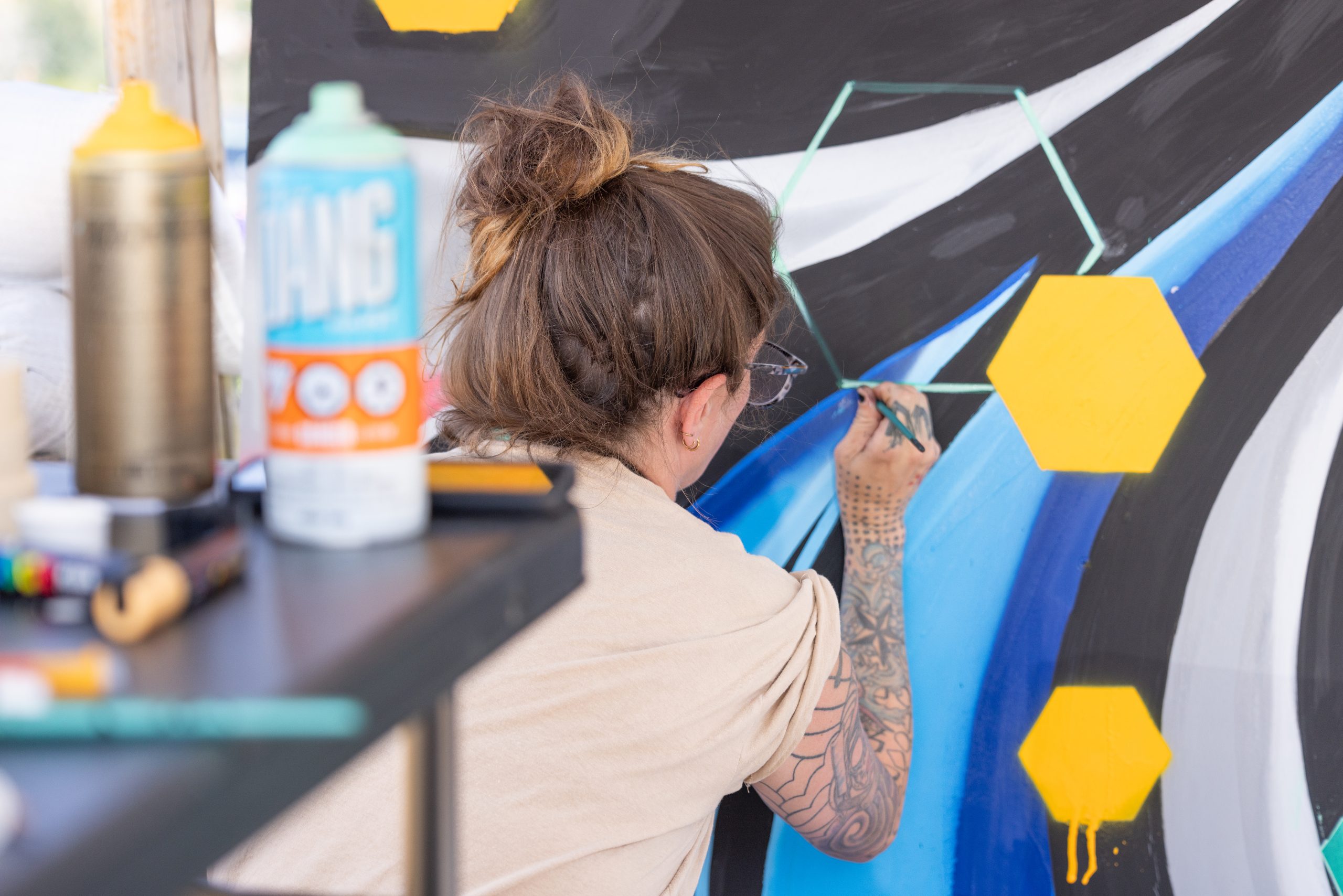 A woman with tattoos paints a colorful abstract mural with geometric shapes in Grand County Colorado.
