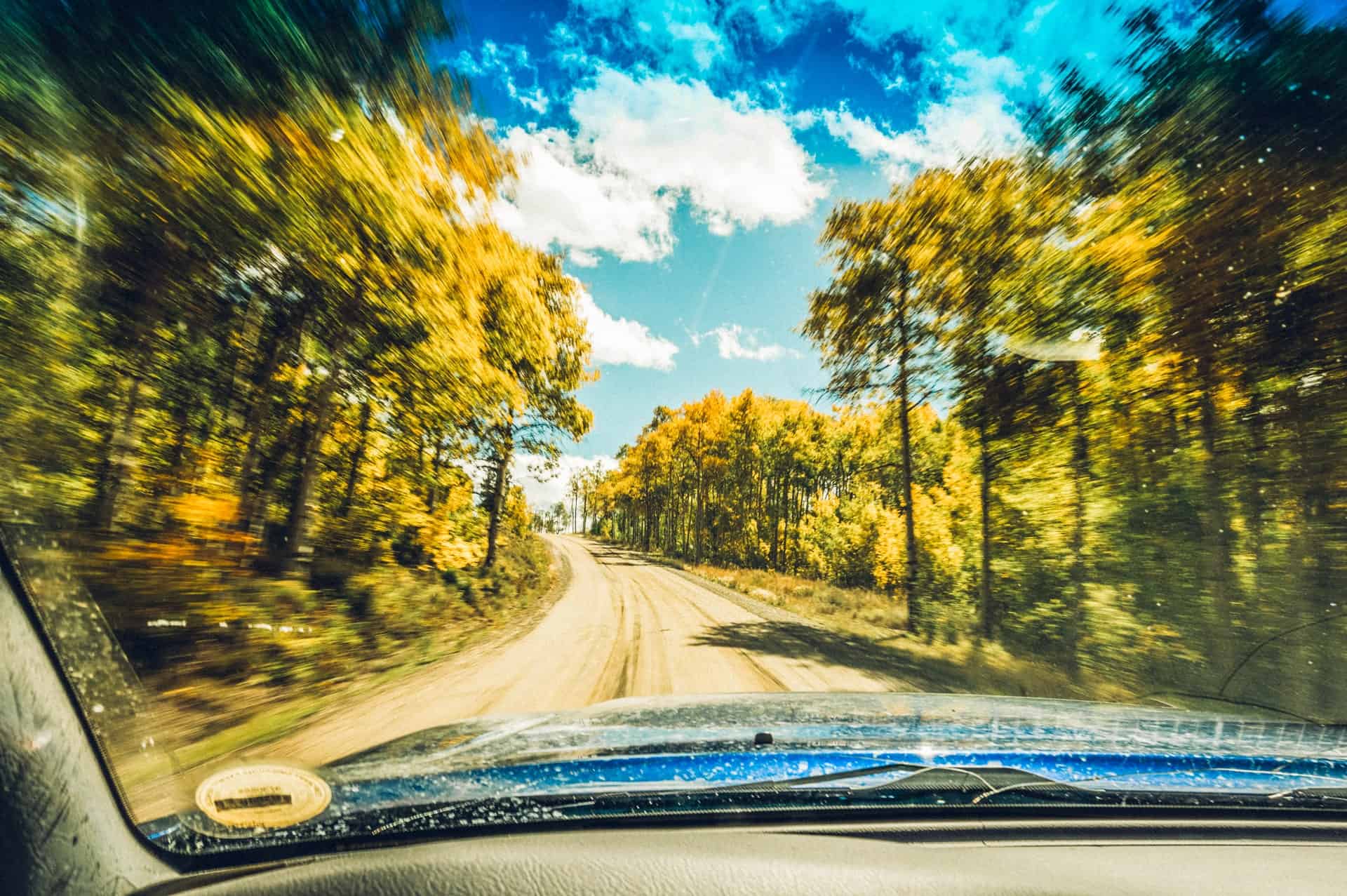 A winding dirt road cuts through a vibrant autumn forest with golden trees in Grand County Colorado.