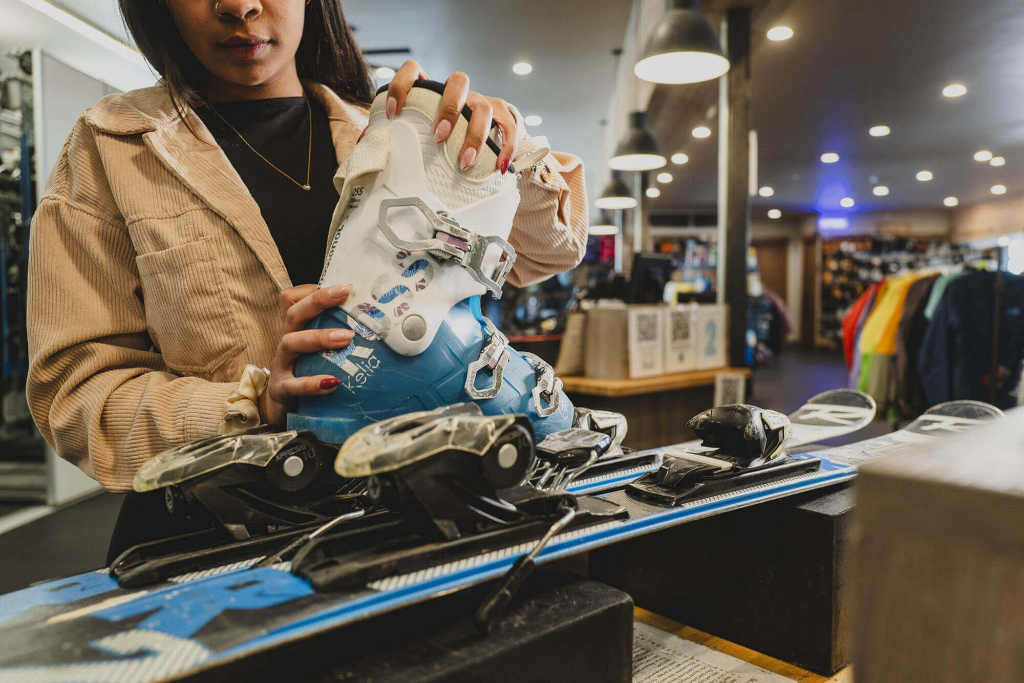 A woman in a beige jacket is adjusting a pair of blue ski boots in a well-lit ski shop in Grand County Colorado.