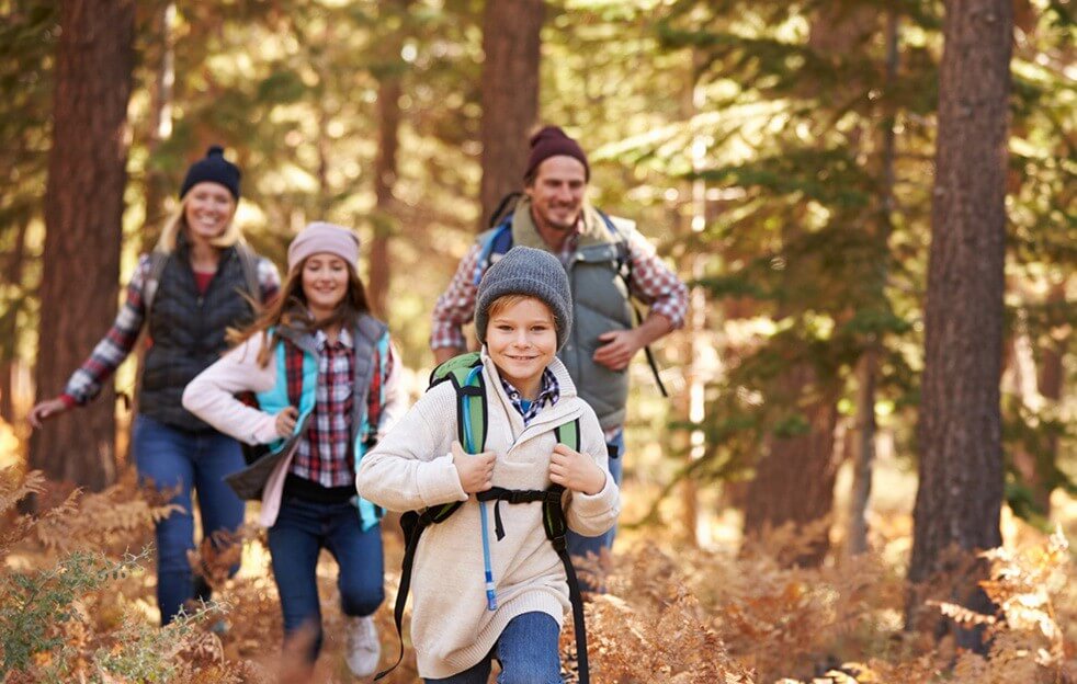 A family of four, dressed in hiking gear, enjoys a walk through a colorful autumn forest in Grand County Colorado.