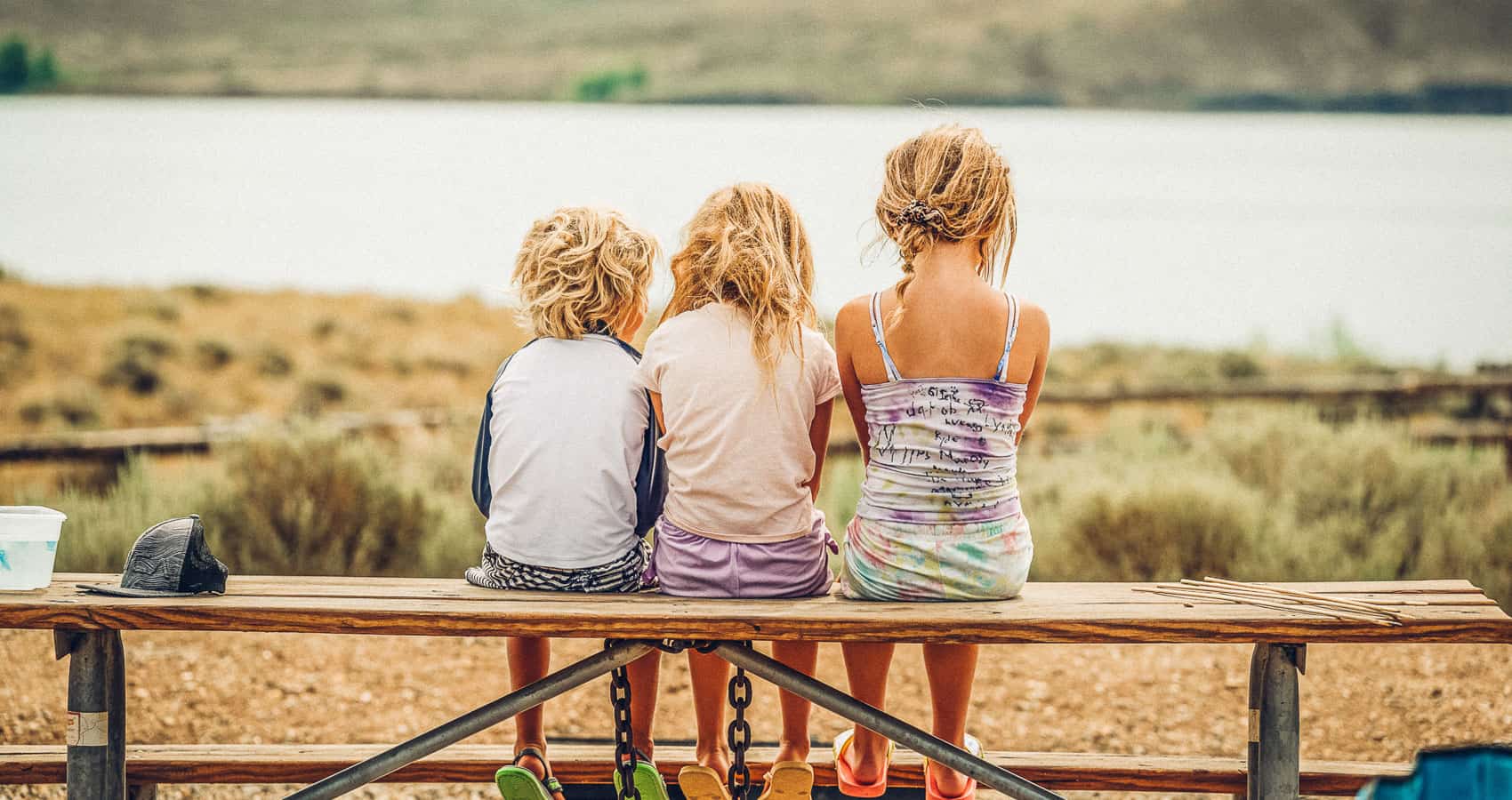 Three children sitting on a picnic bench looking at a lake.