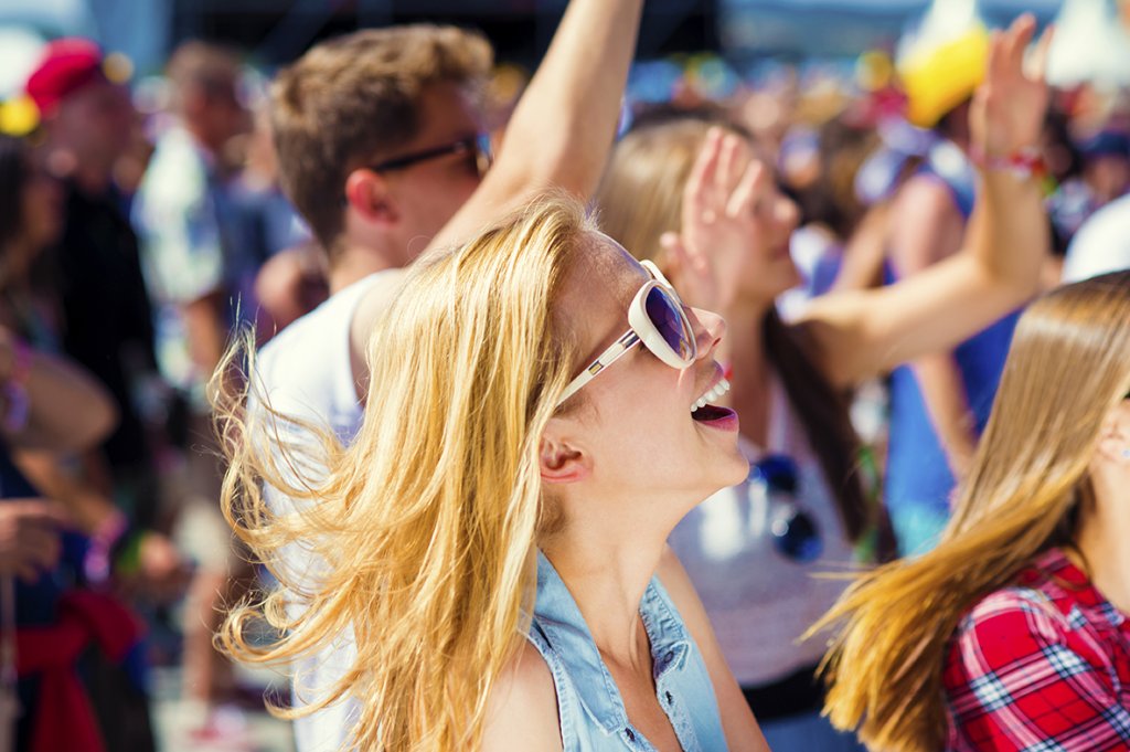 Crowd of people enjoying an outdoor festival, with smiling woman in sunglasses in the foreground.