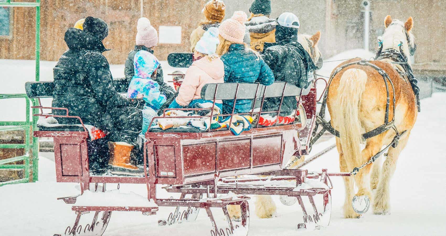 A group of people, bundled in winter clothing, enjoy a horse-drawn sleigh ride through the snow in Grand County Colorado.
