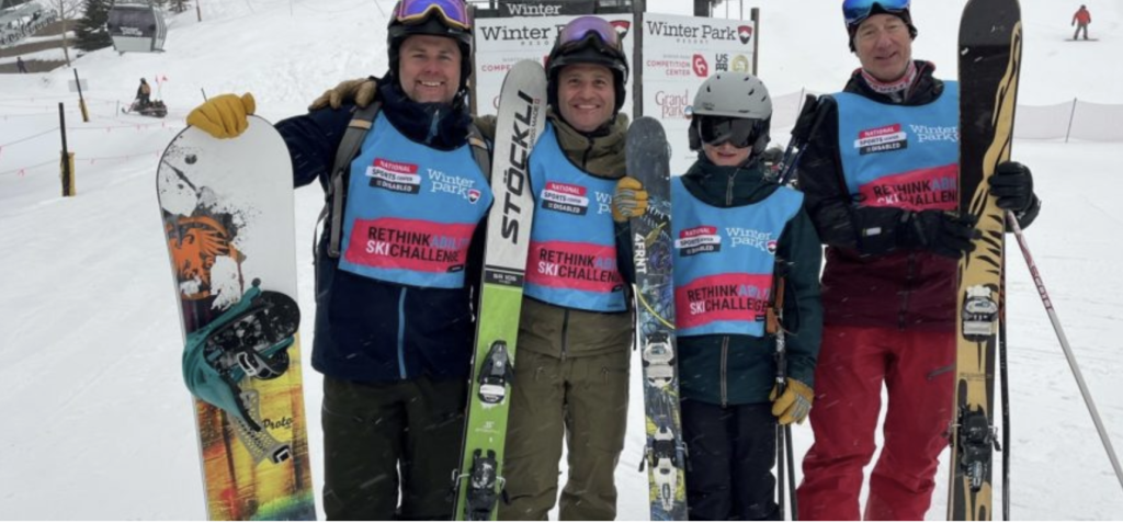 Four skiers and snowboarders pose together on a snowy slope, smiling and holding their equipment in Grand County Colorado.