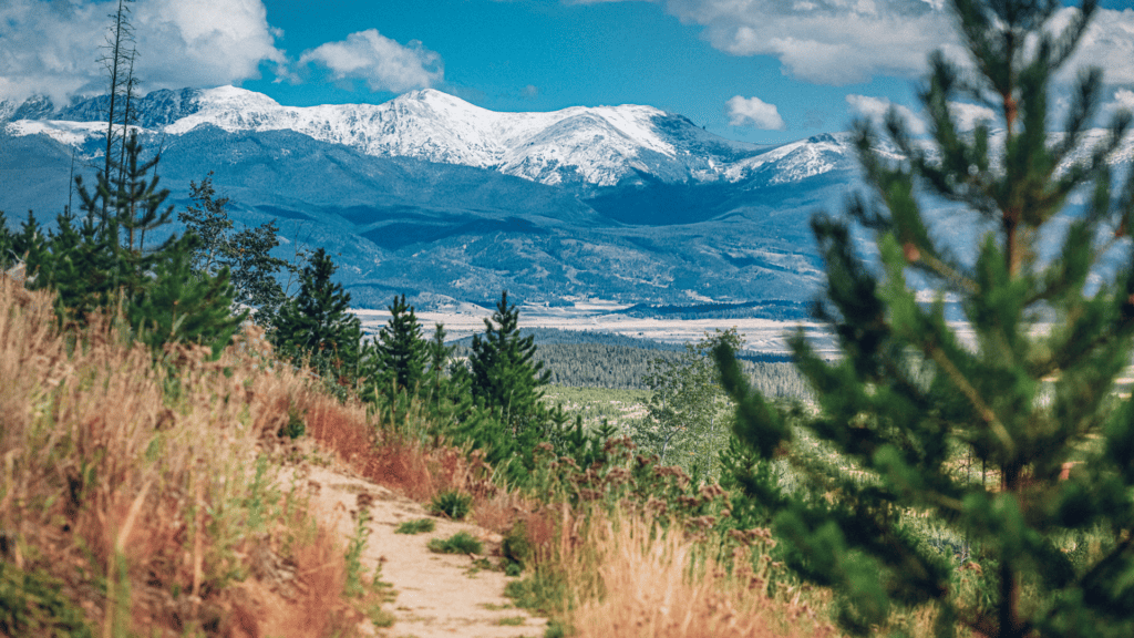 A trail leading to a mountain with snow capped mountains in the background in Fraser, Colorado.