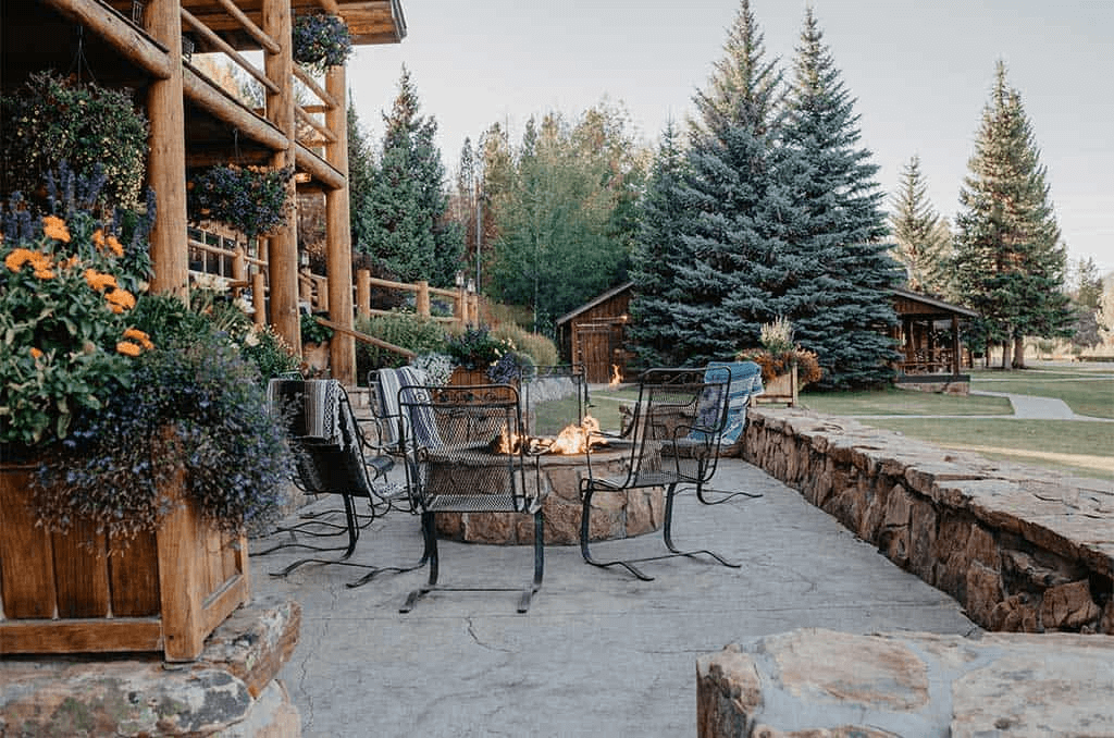 Rustic outdoor patio with stone fireplace, wooden furniture, and hanging flower baskets in Grand County Colorado.