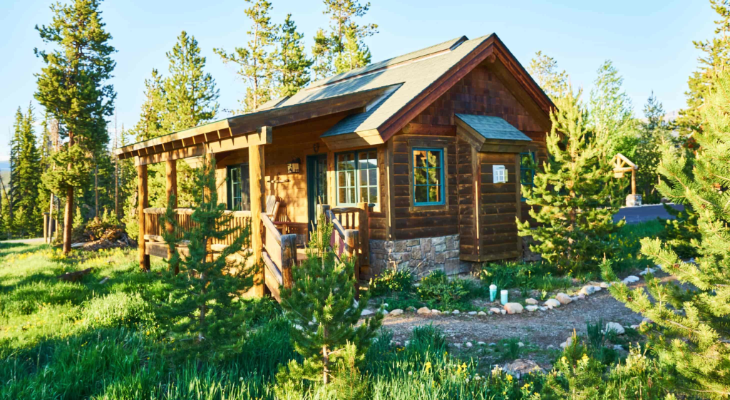 A quaint wooden cabin nestled in a lush green meadow surrounded by tall pine trees in Grand County Colorado.