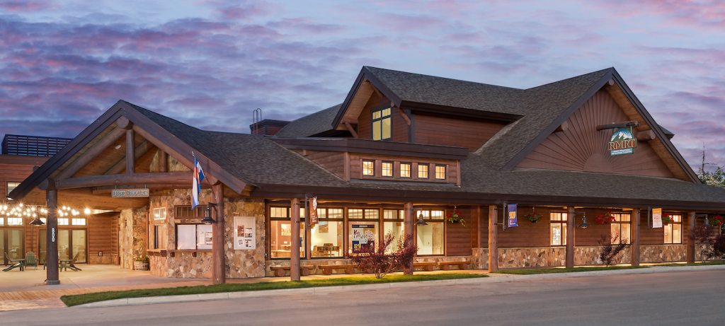 A rustic wooden building with a stone foundation and a large porch, illuminated at dusk in Grand County Colorado.