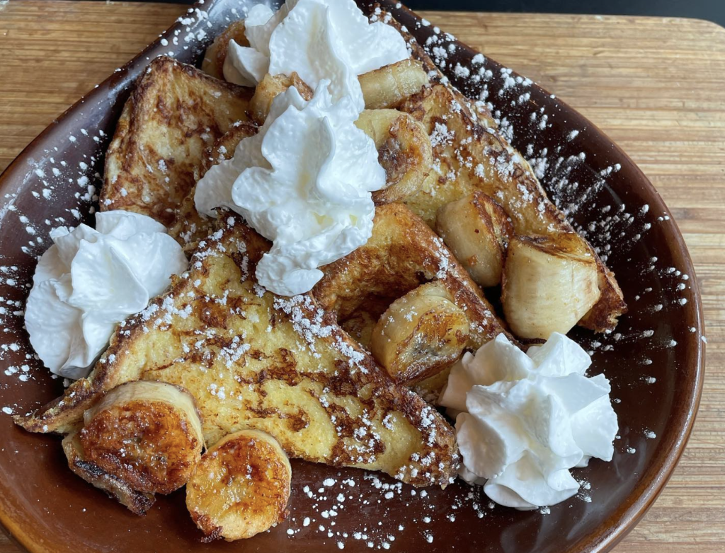 French toast topped with sliced bananas and a dollop of whipped cream on a plate.