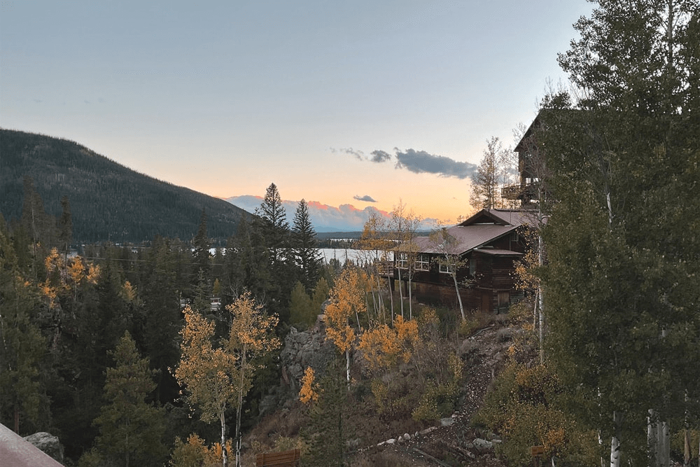 A rustic cabin nestled among autumn trees overlooking a serene lake at sunset in Grand County Colorado.
